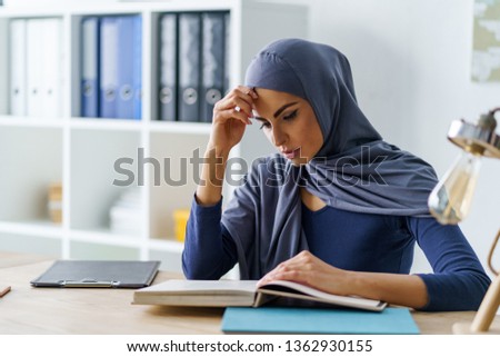 Smart female Muslim student concentrated on reading a book. Studying in university concept.