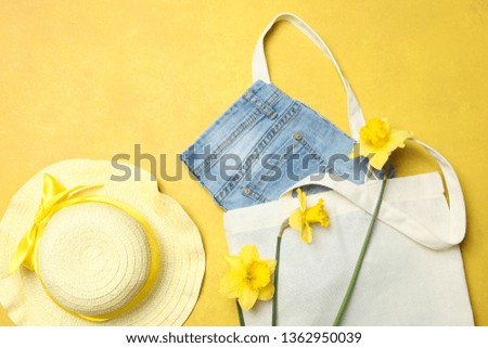 Denim shorts in eco shopping bag, straw beach hat and narcissus on yellow background. Concept summer clothes. Bright colours. Top view, copy space.