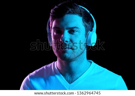 music, technology and people concept - portrait of young man in wireless headphones over ultra violet neon lights in dark room of night club