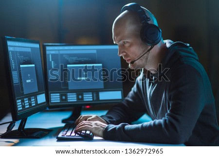 cybercrime, hacking and technology concept - male hacker in headset with progress loading bar on computer screen wiretapping or using virus program for cyber attack in dark room Royalty-Free Stock Photo #1362972965