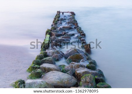 Long exposure photo of old breakwater line in the Baltic sea at sunset.