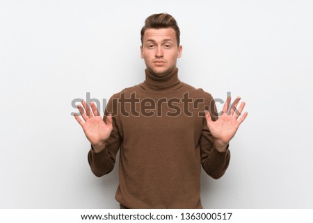 Blonde man over isolated white wall making stop gesture with both hands
