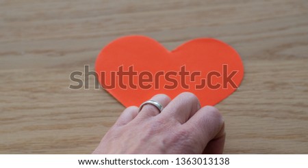 hand with ring on red heard on wooden surface