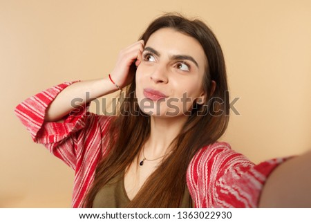 Close up selfie shot of pensive young woman in casual clothes looking aside, putting hand on head isolated on pastel beige background. People sincere emotions, lifestyle concept. Mock up copy space