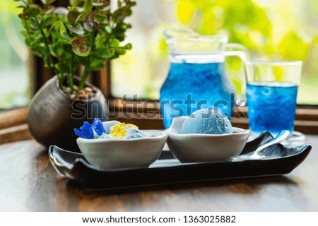 Sweet blue butterfly pea icecream scoop and light blue  sticky rice coconut milk topping with butterfly pea nutritional tea Thai Anchan on wood pattern table and green blur background.