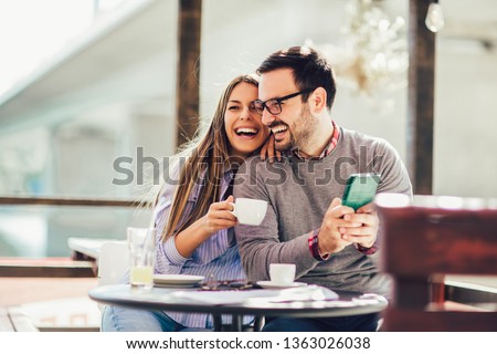Young cheerful man and woman dating and spending time together in cafe, using phone.