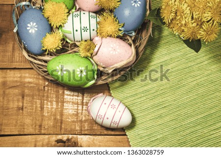 Colorful Easter eggs on wooden background with spring flowers, top view with copy space. Vintage toned photo.