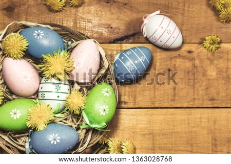Colorful Easter eggs on wooden background with spring flowers, top view with copy space. Vintage toned photo.