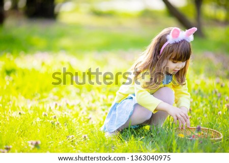 Adorable little girl playing in the garden on Easter egg hunt, searching eggs in the grass at spring april day