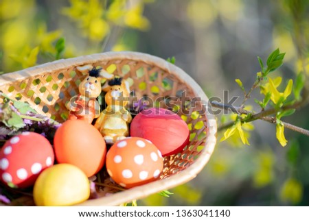 Close up of colorful hand made Easter eggs and little bunnies figurines in a basket outdoors, Easter decorations, cherry blossom
