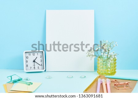 Mockup with blank white frame on blue table against blue wall, alarm, flower in vaze