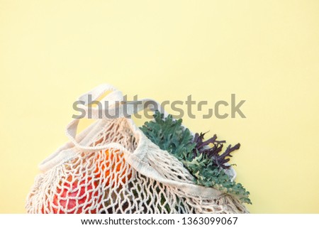 white eco-friendly textile string bag with fresh fruits, herbs and vegetables from local farmer market isolated on yellow background, plastic free shopping, healthy eating, top view