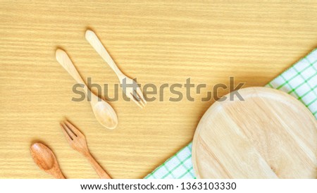 Top view closeup set of wooden cutlery utensil. Wooden fork, spoon, plate on wooden table background. Clean green and white checkered pattern hand towel placed near each other. Kitchen concept.