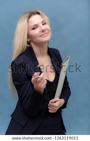 Portrait of happy smiling young cheerful businesswoman standing with folder. Success in business concept studio shot talking to a client. Blue suit. Female model. Blue background. Looking at camera.