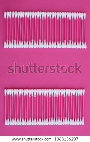 Closeup top view on cotton buds laid in a two horizontal line on pink background.