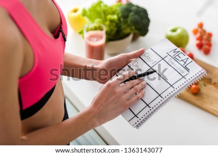 cropped view of sportswoman holding notebook with meal lettering in kitchen 