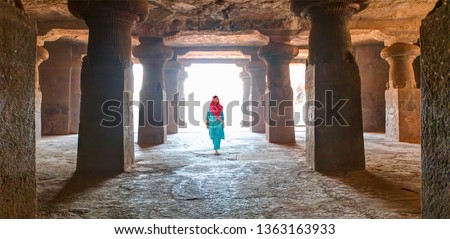 An Indian woman dressed in traditional costume walks in the temple - Hindu sculptures in the cave - Elephanta Island, Mumbai - Maharashtra, India  Royalty-Free Stock Photo #1363163933