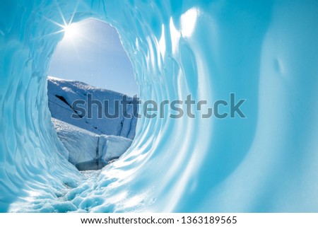 Deep in the Alaskan wilderness, far back on the Matanuska Glacier, the sun shines into the entrance of a large ice cave. The rounded, blue cavern shines with in the sun as the warm light melts the ice