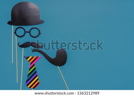Various black photo booth props: cylinder hat, glasses, moustache, smoking pipe, tie on blue background. Greeting card, text HAPPY FATHER'S DAY. Creative composition in minimal style