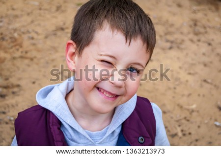 Cute elementary school age six seven year old Caucasian kid squinting and looking at the camera. Outside in the park in the spring or autumn.