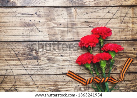 Red carnations and St. George ribbon on wooden background. Symbol may 9, victory day. Copy space