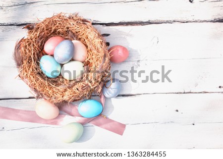 Happy Easter. Colorful Easters eggs in a nest with feathers on the wooden backgound