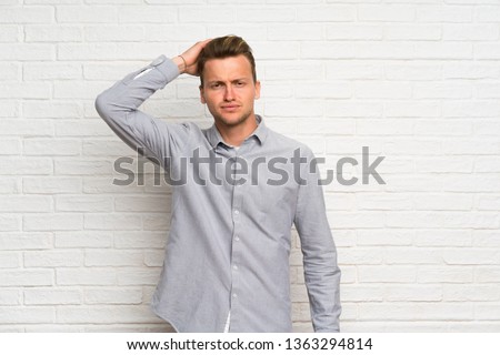 Blonde man over white brick wall with an expression of frustration and not understanding