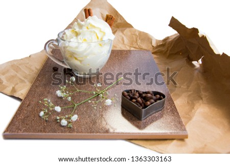  branch of flowers, heart form coffee beans, cinnamon sticks, whipped cream in a glass cup composition in brown tones on crumpled wrapping paper
