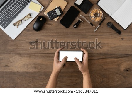 hand touching blank mobile device screen mockup with office accessories on table flat lay.Working on office desk flat lay.Using smartphone device on table.Empty screen mobile phone template.
