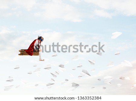 Little sad child in mask and cape floating on book in sky