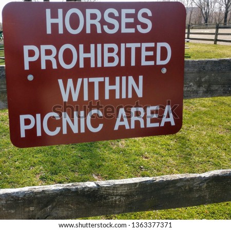 Horses prohibited sign in a parkwith wooden fence and green grass in the background background