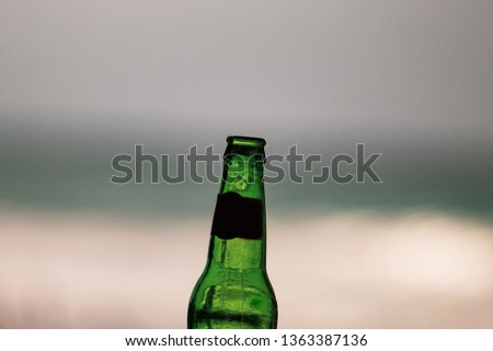 Empty bottle of beer close up, edited; sea view background. iconic image.