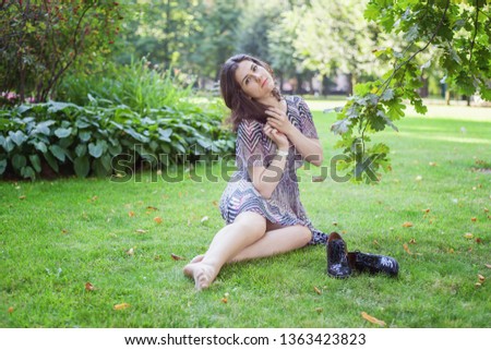 Beautiful young brunete woman with long brown hair resting and smiling on park or garden green background. European woman. Portrait of happy teenage girl relaxing outdoor