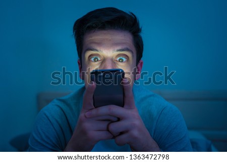 Addicted man chatting and surfing on the Internet with smart phone late at night in bed. Bored, sleepless and tired in dark room with moody light. In insomnia and mobile addiction concept. Royalty-Free Stock Photo #1363472798
