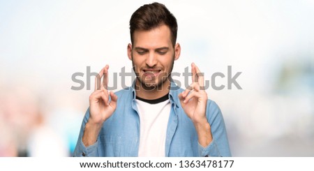 Handsome man with fingers crossing and wishing the best at outdoors
