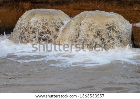 Close-up pictures of water flowing out, flooding two large pipes in the old concrete basin of Thai rural agriculture.