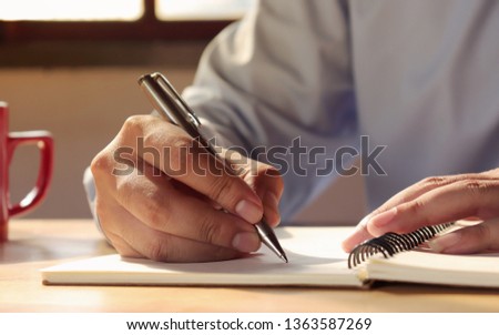 Close-up pictures of a man who wrote a spiral notebook on the table with a coffee mug and writer's idea.