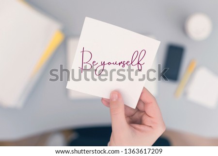 Woman clerk in the office holding paper sticker with the word: Be yourself!  Motivation concept  