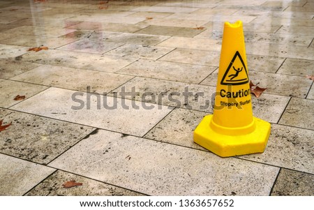 Yellow cone with caution slippery surface sign, on wet pavement tiles.