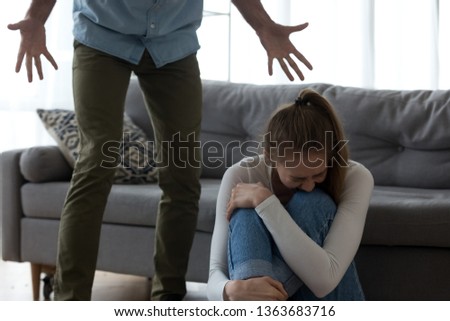 Unhappy frightened woman crying, sitting on floor, aggressive man shouting to scared wife, angry husband emotionally quarreling, arguing, emotional psychological abuse, domestic violence concept Royalty-Free Stock Photo #1363683716