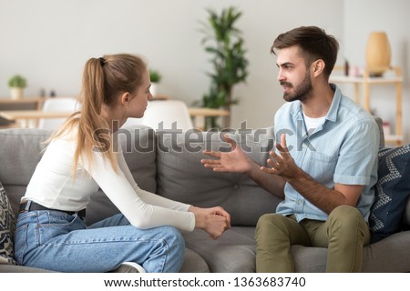 Serious young couple sitting together on sofa, talking about relationships, spending time together at home, focused wife listening to speaking husband, friends having conversation Royalty-Free Stock Photo #1363683740