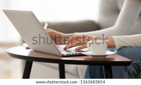 Close up woman using laptop, sitting on sofa, female hands typing, writing notes, studying languages, distance learning concept, checking email in morning, drink coffee, working at home Royalty-Free Stock Photo #1363683854