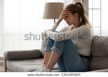 Upset woman frustrated by problem with work or relationships, sitting on couch, embracing knees, covered face in hand, feeling despair and anxiety, loneliness, having psychological trouble Royalty-Free Stock Photo #1363683869