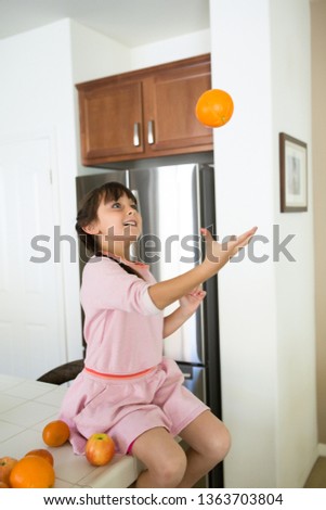 playful girl with oranges sitting on kitchen counter top. 