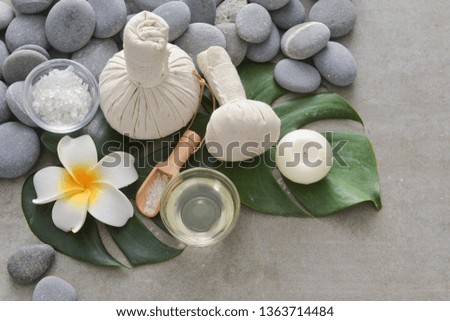 spa composition with monstera leaves ,salt in bowl, spoon, Plumeria ,candle , ,herbal,ball ,salt in bowl, pile of gray stones
