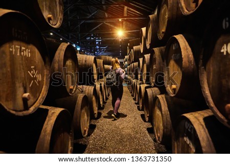Young woman tourist  walk in old aged traditional wooden barrels with wine in a vault lined up in cool and dark cellar in Italy, Porto, Portugal, France