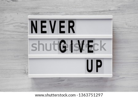 'Never give up' words on lightbox over white wooden background. Flat lay, from above, overhead. Close-up.
