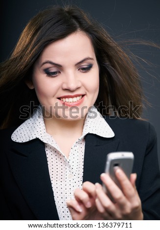 Attractive young woman in a black jacket. Woman holding a mobile phone and looks at it. On a gray background