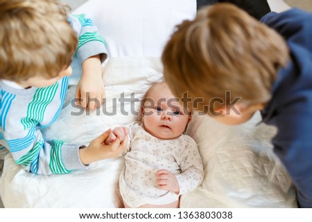 Two little kids boys with newborn baby girl, cute sister. Siblings. Brothers and baby playing with colorful toys and rattles together. Kids bonding. Family of three bonding, love