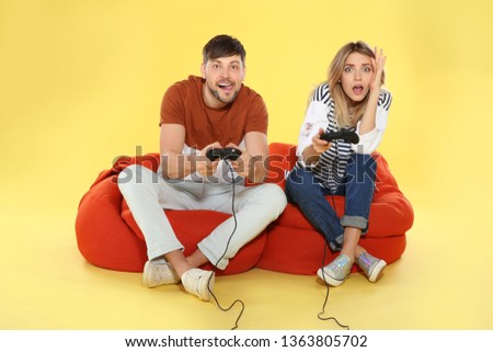 Emotional couple playing video games with controllers on color background